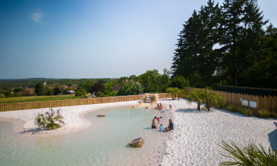 Families relaxing by the natural lagoon-style pool at Camping Le Séquoïa in Payrac, Dordogne.