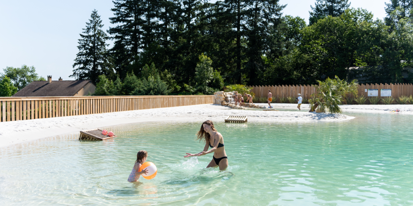 Mother and child playing in the crystal-clear natural lagoon pool at Camping Le Séquoïa in Payrac, in the heart of the Lot and Dordogne Valley.
