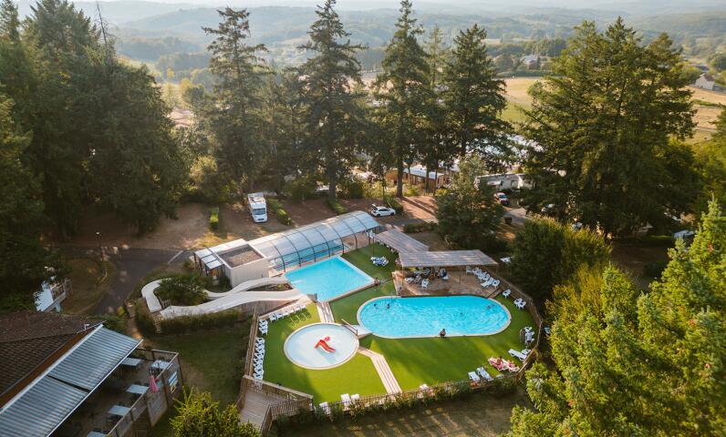Aerial view of the swimming pool complex at Camping Le Séquoïa surrounded by trees in the Dordogne Valley.