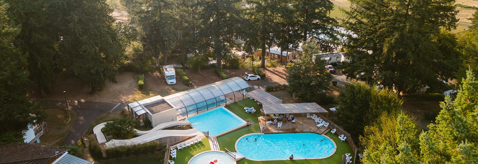 Aerial view of the swimming pool complex at Camping Le Séquoïa surrounded by trees in the Dordogne Valley.