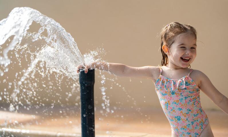 Little girl playing with the water fountain in the children’s splash pool at Camping Le Séquoïa.