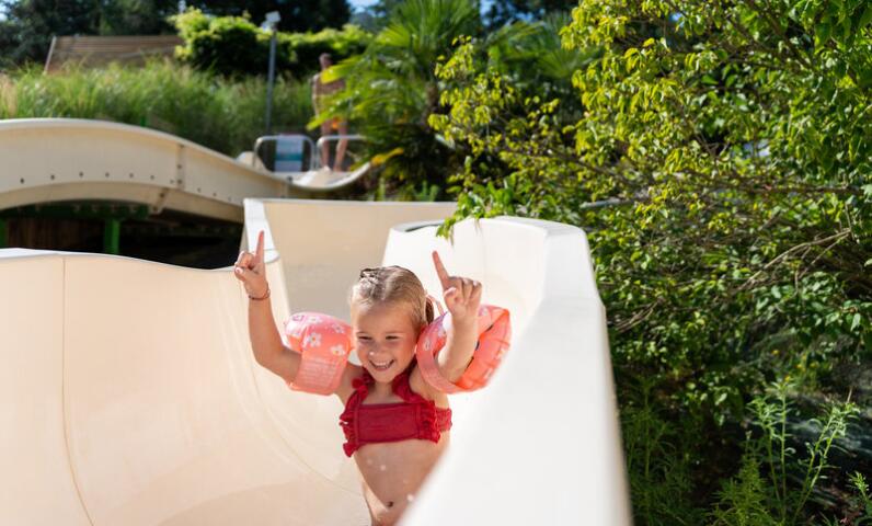 Smiling child going down the water slide at Camping Le Séquoïa, enjoying a sunny day in the Dordogne Valley.