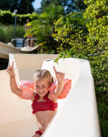 Smiling child going down the water slide at Camping Le Séquoïa, enjoying a sunny day in the Dordogne Valley.
