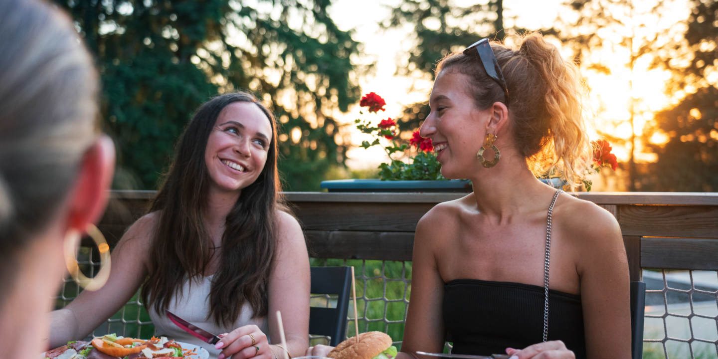 Two friends enjoying dinner at the restaurant terrace of Camping Le Séquoïa at sunset in the Dordogne Valley.