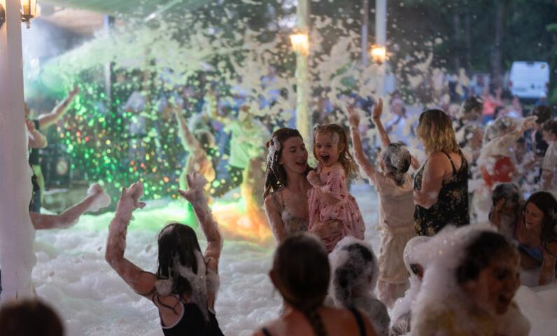 Family foam party at Camping Le Séquoïa with children and parents dancing in the bubbles.