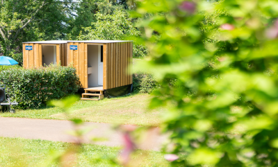Private wooden bathroom cabin on a camping pitch surrounded by greenery at Camping Le Séquoïa in Payrac, Dordogne.