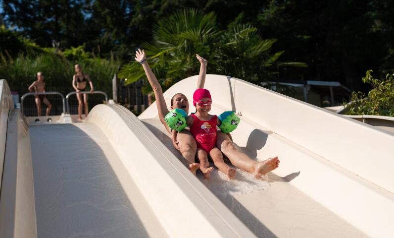 Two people sliding together on an outdoor water slide, enjoying a sunny moment in the campsite’s aquatic area.