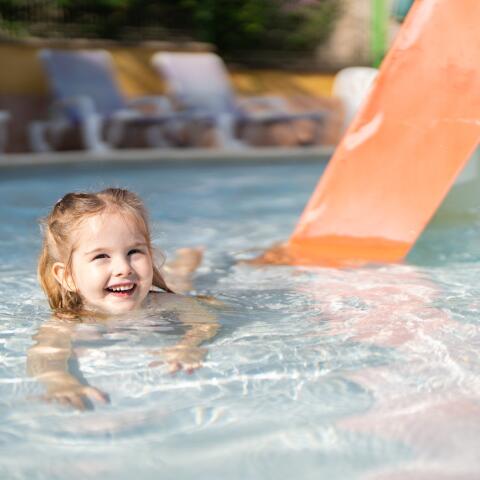 Smiling young child playing in a shallow paddling pool with a small slide, in a safe and family-friendly aquatic area.