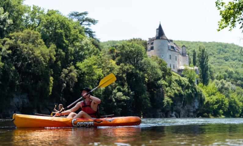 Couple canoeing on the Dordogne River near a castle, enjoying the sunshine and scenic views close to Camping Le Séquoïa.