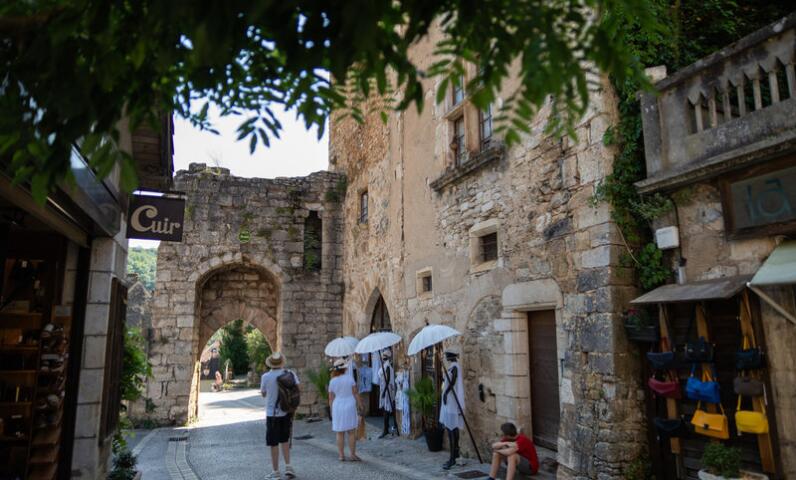 Street scene in Rocamadour featuring stone buildings, a medieval gateway and visitors walking in the summer light of this iconic village in the Lot.