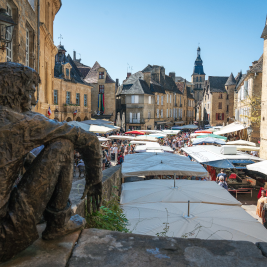 Vue sur le marché de Sarlat-la-Canéda avec la statue de La Boétie au premier plan, entourée de bâtiments médiévaux de la vallée de la Dordogne.