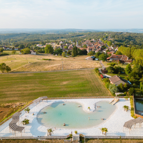 Vue aérienne du lagon naturel entouré de campagne au Camping Le Séquoïa à Payrac, au cœur de la vallée du Lot et de la Dordogne.