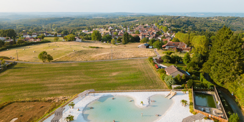 Vue aérienne du lagon naturel entouré de campagne au Camping Le Séquoïa à Payrac, au cœur de la vallée du Lot et de la Dordogne.