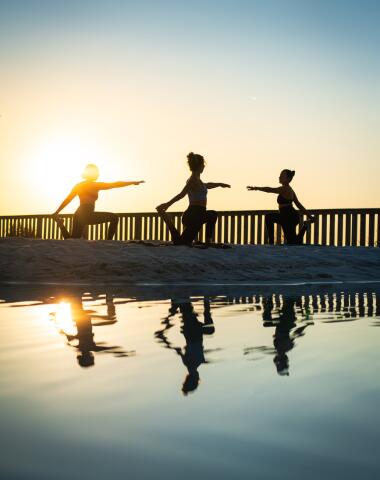 Vacancières pratiquant le yoga au bord de la lagune au coucher du soleil au Camping Le Séquoïa, entourées de nature et de calme.