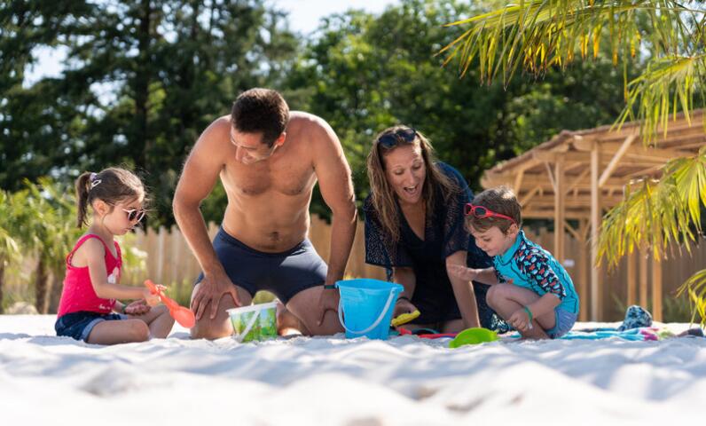 Famille avec de jeunes enfants jouant dans le sable au bord de la lagune naturelle du Camping Le Séquoïa, dans la Vallée de la Dordogne.