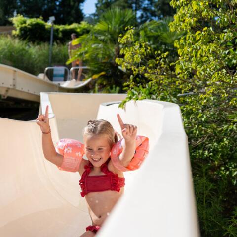 Enfant souriant descendant le toboggan aquatique au Camping Le Séquoïa, profitant d’une journée ensoleillée dans la Vallée de la Dordogne.