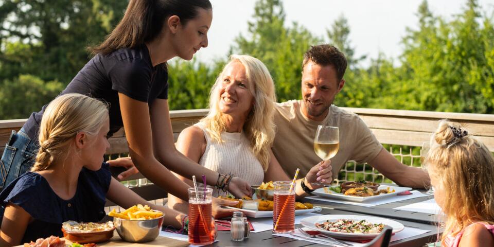 Famille profitant d’un déjeuner en terrasse au restaurant du Camping Le Séquoïa avec vue sur la nature environnante.