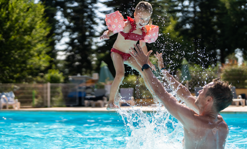 Père jouant avec son enfant dans la piscine du Camping Le Séquoïa par une journée ensoleillée en Dordogne.