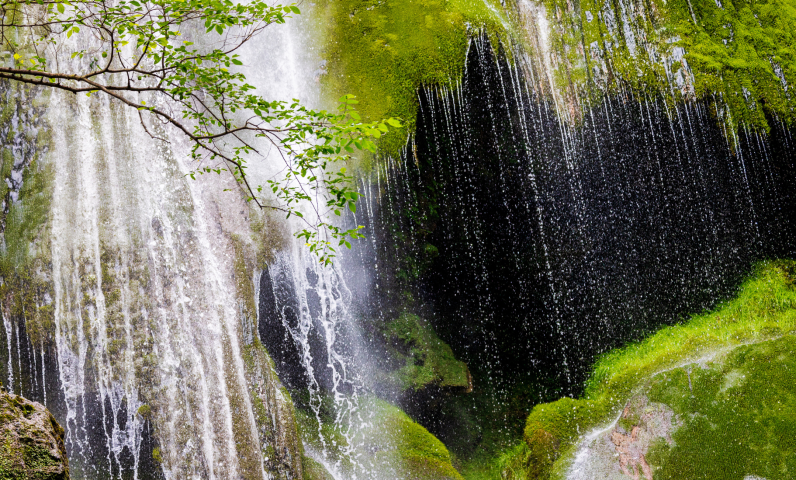 Gros plan sur la cascade d’Autoire, avec des filets d’eau tombant sur des rochers couverts de mousse et une végétation verdoyante, dans un cadre naturel paisible.