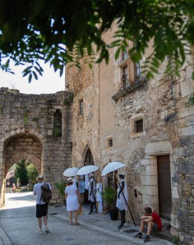 Scène de rue à Rocamadour avec des bâtiments en pierre, une ancienne porte médiévale et des visiteurs se promenant sous une lumière estivale dans ce village emblématique du Lot.