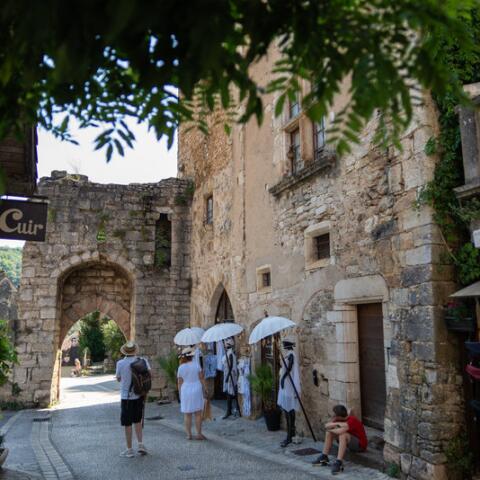 Scène de rue à Rocamadour avec des bâtiments en pierre, une ancienne porte médiévale et des visiteurs se promenant sous une lumière estivale dans ce village emblématique du Lot.