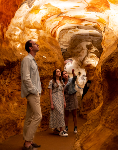 Famille visitant une grotte reconstituée de Lascaux IV, admirant les parois rocheuses et les peintures préhistoriques dans un espace muséographique immersif en Dordogne.