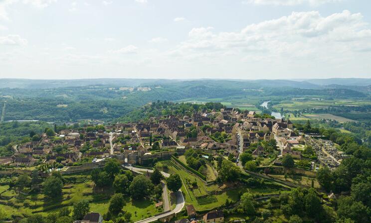 Vue aérienne du village perché de Domme dominant la vallée de la Dordogne, avec ses remparts, ses maisons en pierre et les paysages verdoyants environnants.