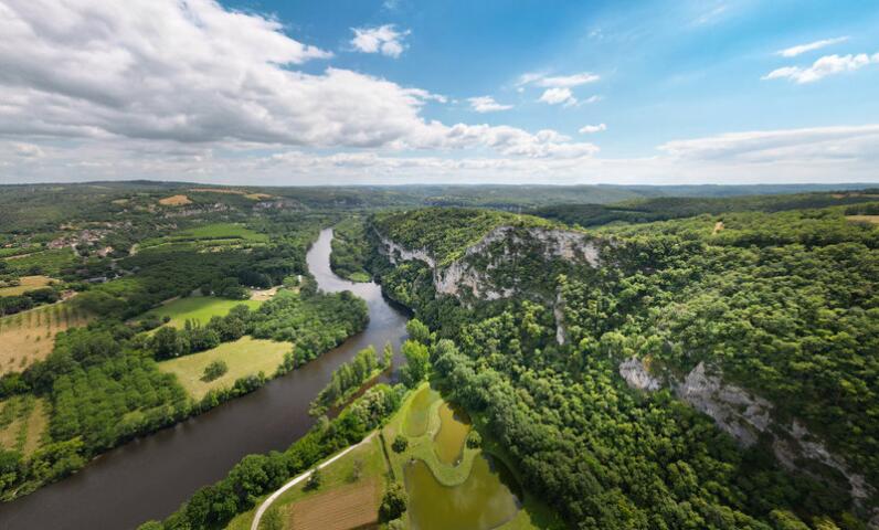 Vue aérienne de la rivière Dordogne serpentant à travers la vallée verdoyante de Saint-Sozy, avec falaises calcaires, forêts et paysages naturels typiques de la Dordogne.