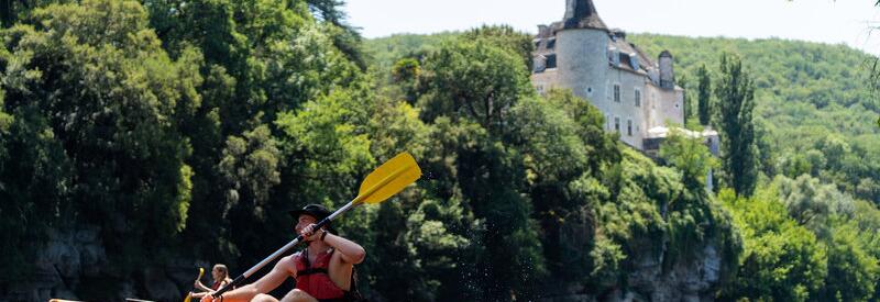 Couple faisant du canoë sur la Dordogne près d’un château, profitant du soleil et des paysages à proximité du Camping Le Séquoïa.