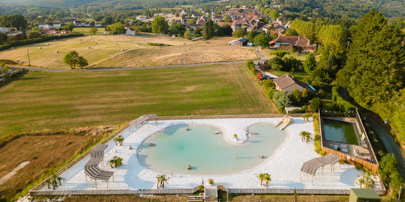 Vue aérienne du lagon naturel entouré de campagne au Camping Le Séquoïa à Payrac, au cœur de la vallée du Lot et de la Dordogne.