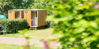 Houten privé sanitaircabine op een kampeerplaats, omgeven door groen op Camping Le Séquoïa in Payrac, Dordogne.