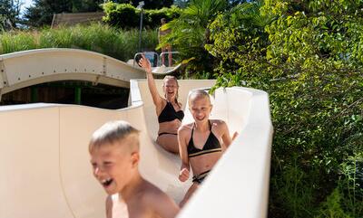 Kinderen die plezier maken op een waterglijbaan in een natuurlijk gelegen waterpark, lachend en genietend van de zon.