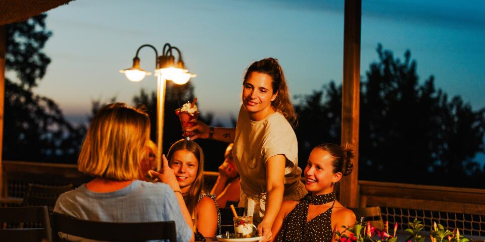 Een gezin geniet van een diner op het terras van het restaurant van Camping Le Séquoïa