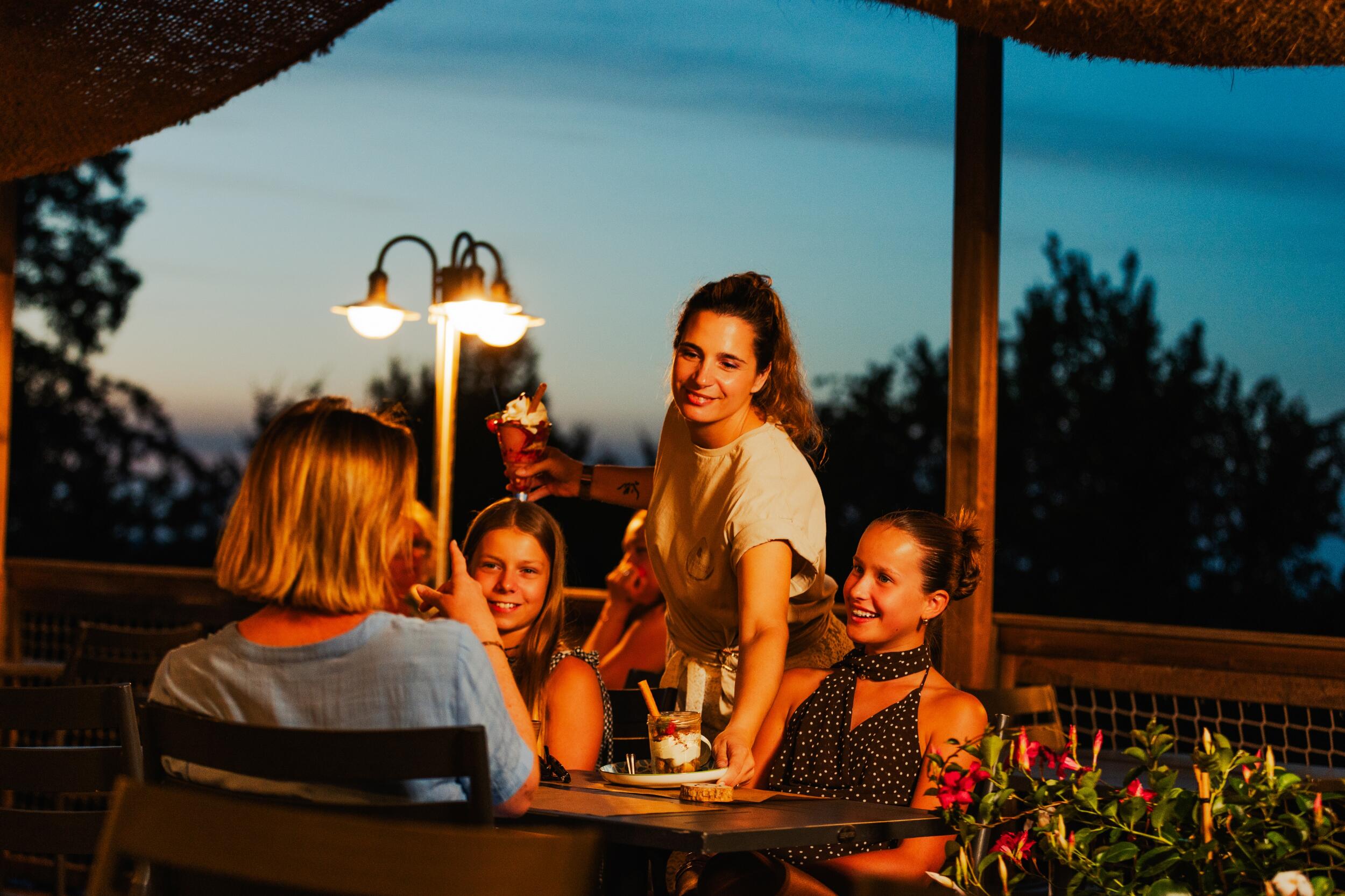 Gezin geniet samen van een maaltijd op het terras van Camping Le Séquoïa
