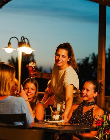 Gezin geniet samen van een maaltijd op het terras van Camping Le Séquoïa