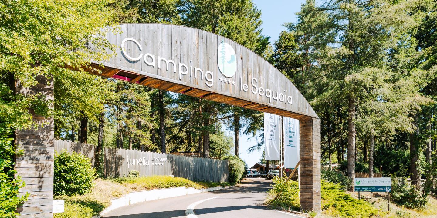 Ingang van Camping Le Séquoïa met de welkomstboog tussen de bomen